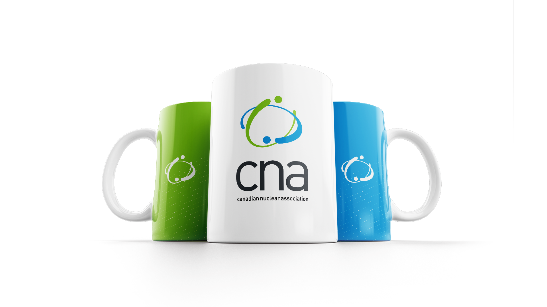White mug with full-colour CNA logo centered on the front, in front of green and blue mugs each featuring the white CNA logo mark.